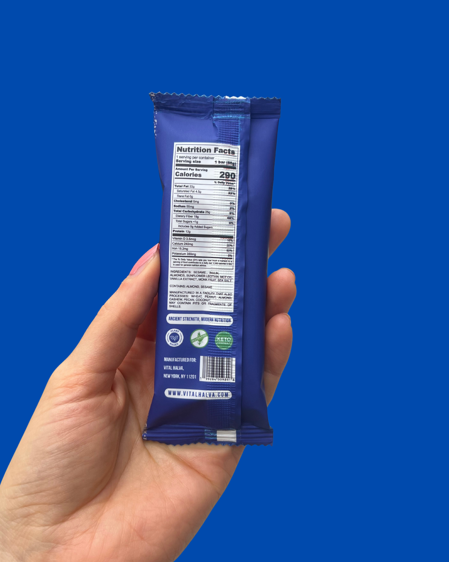 Hand holding a blue snack bar package against a blue background