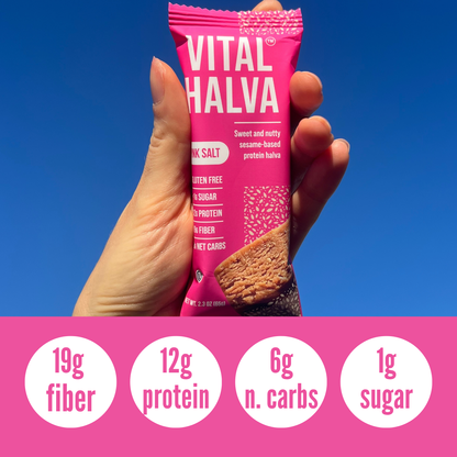 Hand holding a pink 'Vital Halva' bar with nutritional information on a blue background